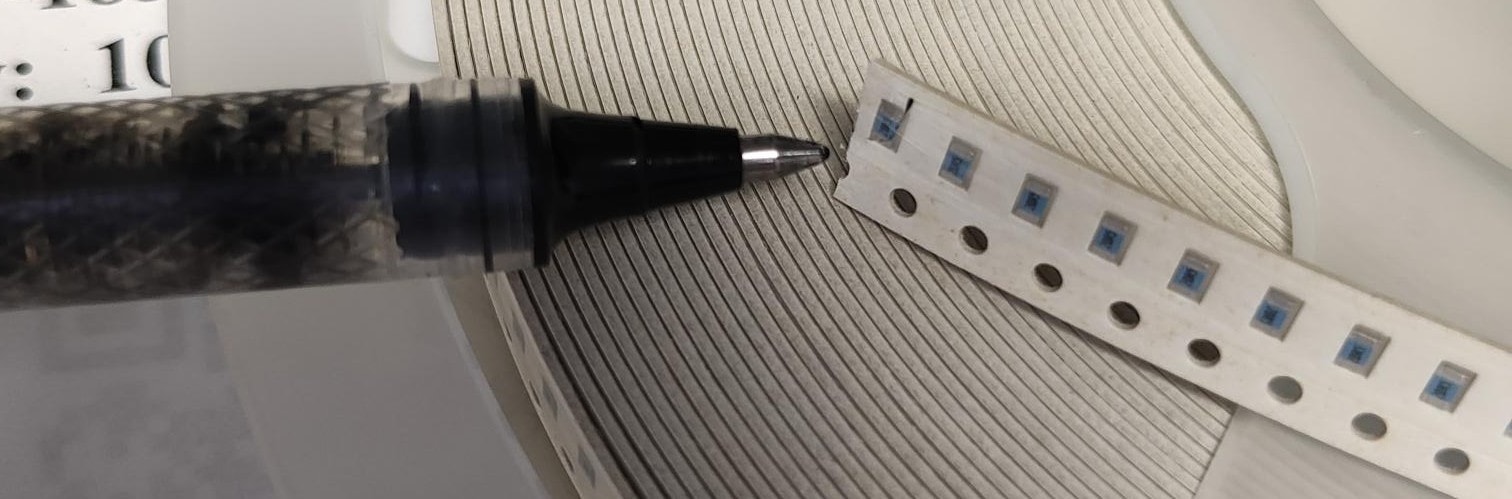 SMT surface-mount resistors on tape reel next to a pen for scale